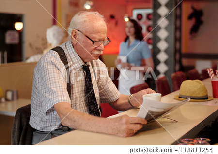 Elderly Man Reading Newspaper in Cozy Coffee Shop Elderly Man Reading Newspaper in Cozy Coffee Shop 118811253