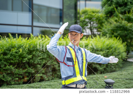 A male security guard directing traffic with a whistle signal 118812966