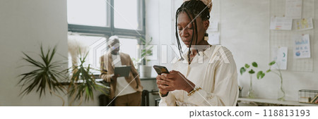 Website banner of African American businesswoman checking social media while her coworker using tablet in background Website banner of African American businesswoman checking social media while her coworker using tablet in background 118813193