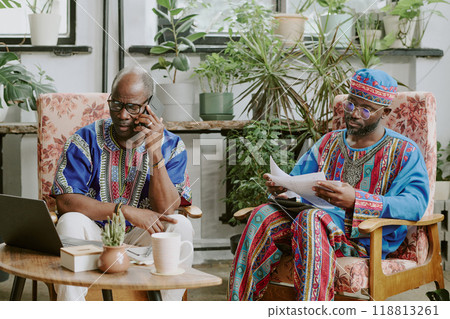 Mature African American worker speaking on phone while his colleague reading report during break time 118813261