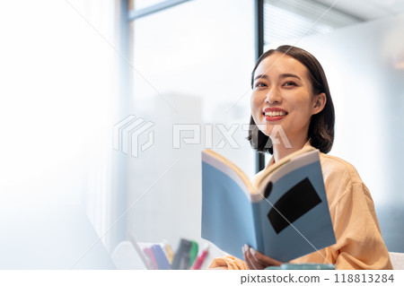 A woman smiling while working on a computer with a book in hand 118813284