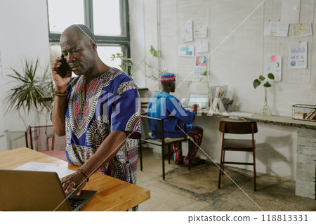 African American businessman speaking on phone with hi partner while his worker making financial presentation in background African American businessman speaking on phone with hi partner while his worker making financial presentation in background 118813331