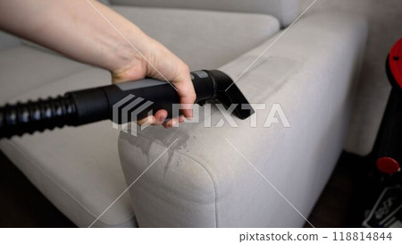 Woman is cleaning sofa with vacuum cleaner at home 118814844