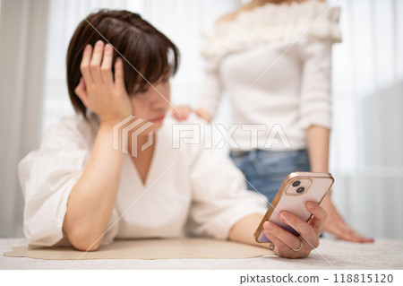 一位女士站在一位正在看智慧型手機的女士旁邊 一位女士站在一位正在看智慧型手機的女士旁邊 118815120