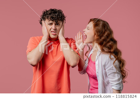 Grumpy woman quarrels on husband or boyfriend On pink. Tired man covers ears 118815824