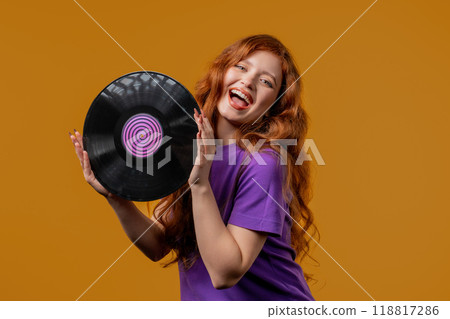 Positive red haired woman with vinyl record disc on yellow. Hobby, music lover, collection, nostalgia lifestyle Positive red haired woman with vinyl record disc on yellow. Hobby, music lover, collection, nostalgia lifestyle 118817286