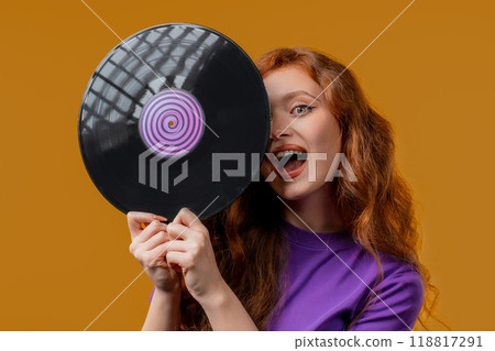 Positive red haired woman with vinyl record disc on yellow. Hobby, music lover, collection, nostalgia lifestyle 118817291