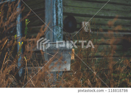 A bucket hangs on a chain against the background of an old, rustic house 118818786