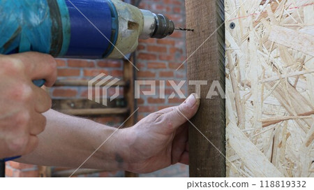 close up of male working hands with drill making hole in wooden material structure, building cage for domestic quails using drilling and fasteners 118819332