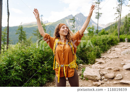 Young female traveler with hiking poles, bright backpack enjoys mountain scenery. Active lifestyle. Young female traveler with hiking poles, bright backpack enjoys mountain scenery. Active lifestyle. 118819839