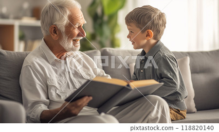 An old man and a young boy are sitting on a couch reading a book together. The man is smiling and the boy is laughing. Concept of warmth and happiness 118820140