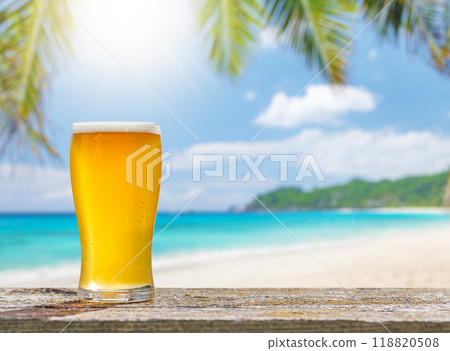 A glass of cold beer sits on a table with a beautiful sea view A glass of cold beer sits on a table with a beautiful sea view 118820508