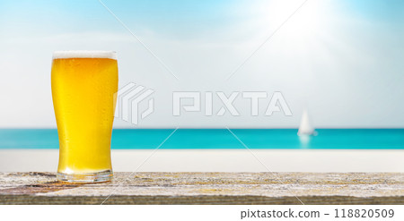 A glass of cold beer sits on a table with a beautiful sea view 118820509