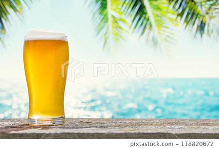 A glass of cold beer sits on a table with a beautiful sea view 118820672