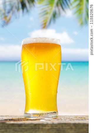 A glass of cold beer sits on a table with a beautiful sea view 118820676