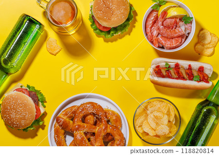 A vibrant photo showcasing a glass of beer surrounded by various snacks and fast food 118820814