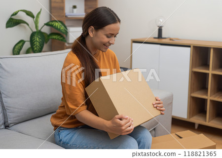 Cheerful woman inspects box with parcel with things from online Internet store female wants to open cardboard packaging with goods in premise of accommodation Cheerful woman inspects box with parcel with things from online Internet store female wants to open cardboard packaging with goods in premise of accommodation 118821365
