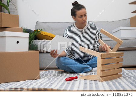 New owner with serious emotion holds instruction sitting among various decorations in boxes for house after moving to contemporary apartment with spacious territory 118821375