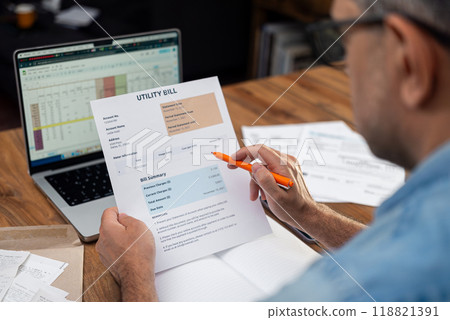 Middle aged man with pen reads utility bill over notebook near laptop, male entrepreneur calculates expenditures for service in company office, regular payments growth Middle aged man with pen reads utility bill over notebook near laptop, male entrepreneur calculates expenditures for service in company office, regular payments growth 118821391