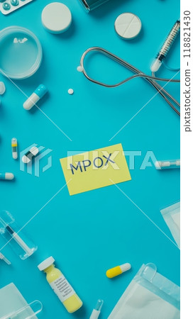 Yellow 'Mpox' label surrounded by pills and medical supplies on a blue background. Medical treatment and outbreak control concept. 118821430