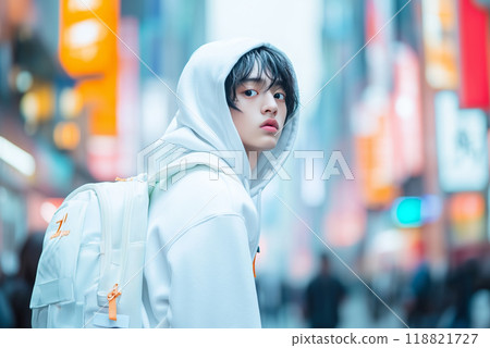 Young person in white hoodie stands in bustling city street with vibrant neon signs at dusk 118821727