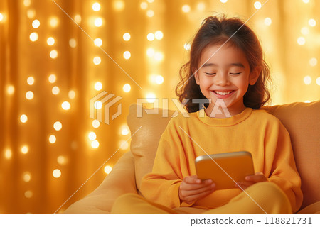Young girl smiling while using her smartphone in a cozy, brightly lit room adorned with warm lights 118821731