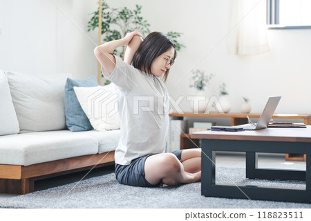 一位女士在客廳一邊看著電腦一邊伸展身體 一位女士在客廳一邊看著電腦一邊伸展身體 118823511