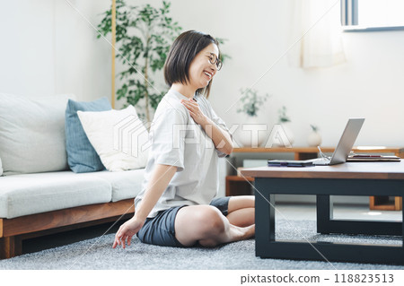 A woman stretching while looking at a laptop in her living room at home 118823513