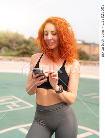 Happy sporty woman using smartphone while standing Happy sporty woman using smartphone while standing 118823605