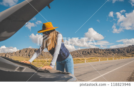 A woman in a cowboy hat is standing next to a car with the hood up. traveling through the peruvian andes A woman in a cowboy hat is standing next to a car with the hood up. traveling through the peruvian andes 118823946