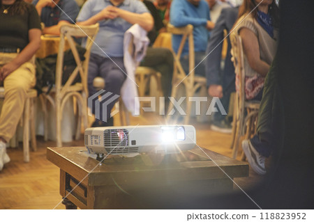 A projector is on a table in front of a group of people A projector is on a table in front of a group of people 118823952