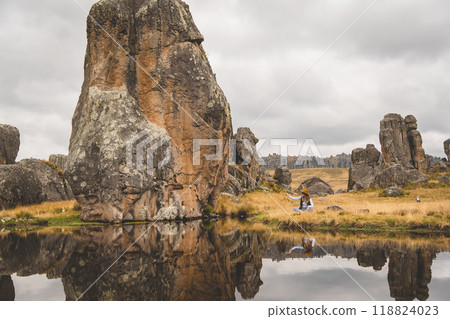 A woman sits in a field next to a river, tourist in the peruvian andes, Huaillay, Pasco, Peru. 118824023