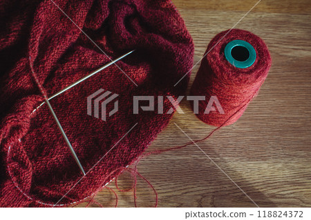 Cherry coloured wool yarn bobbin with knitting needles. Dark red wool and knitting on wooden table. Knitting hobby. Knitwear concept. Needlework design. Knitters concept. Cherry coloured wool yarn bobbin with knitting needles. Dark red wool and knitting on wooden table. Knitting hobby. Knitwear concept. Needlework design. Knitters concept. 118824372