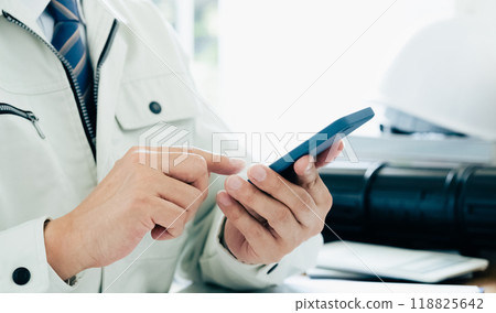 The hands of a man in work clothes operating a smartphone 118825642