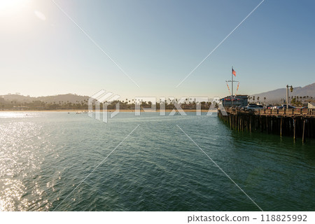 A beautiful pier near the water has majestic mountains behind it 118825992