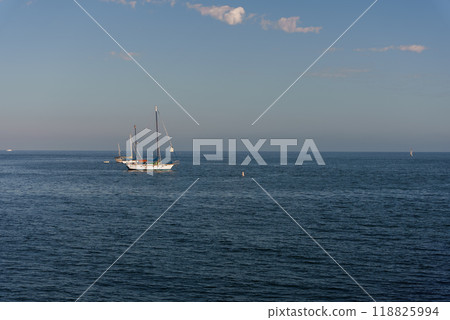 A sailboat is peacefully floating on top of a vast body of water A sailboat is peacefully floating on top of a vast body of water 118825994