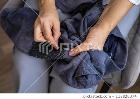 A woman sews up a hole in her children's knitted pants. Sews a patch onto a hole in the knees.  118826374