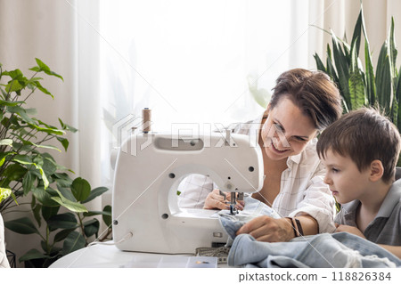 Mom and son are repairing old torn jeans using a sewing machine. A woman teaches a boy to sew. 118826384