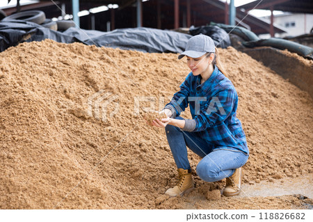 Female farmer squatting at large heap of brewer's spent grain Female farmer squatting at large heap of brewer's spent grain 118826682
