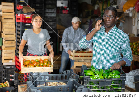 Owner of vegetable warehouse is talking on mobile phone while other workers are sorting vegetables 118826887