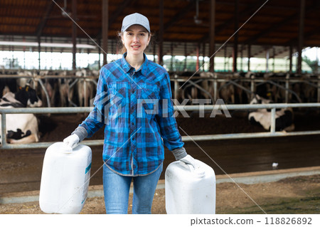 Woman farmer with plastic canisters in cowshed 118826892