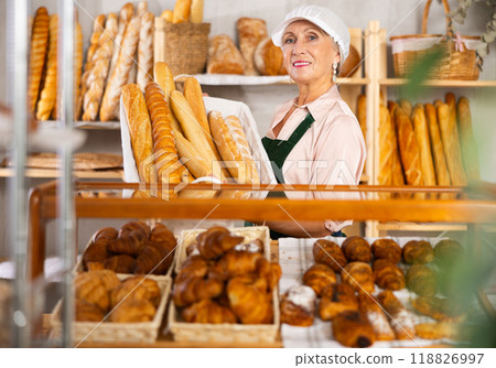 Senior female baker worker sells baguette, shows many products Senior female baker worker sells baguette, shows many products 118826997