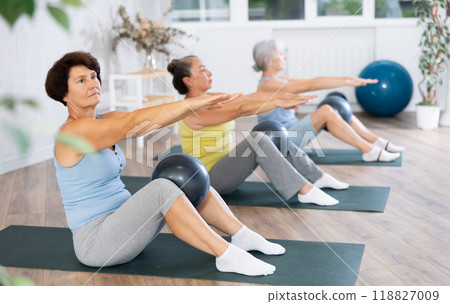 Elderly women perform softball exercises sitting on floor, workout for beautiful figure, toned body Elderly women perform softball exercises sitting on floor, workout for beautiful figure, toned body 118827009