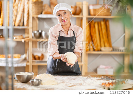 Senior woman works in bakery as baker, kneads dough, works with flour. 118827046
