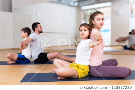 Tween girl with mother doing exercises in pair during family yoga workout Tween girl with mother doing exercises in pair during family yoga workout 118827220