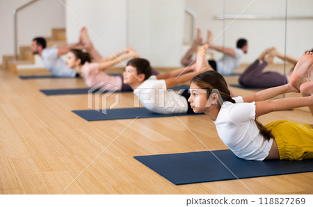 Teen girl doing asana Dhanurasana during family yoga workout at gym 118827269