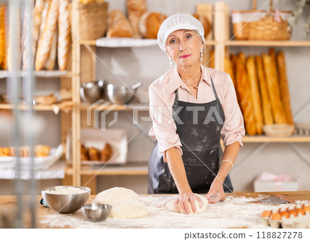 Senior woman works in bakery as baker, kneads dough, works with flour. Senior woman works in bakery as baker, kneads dough, works with flour. 118827278
