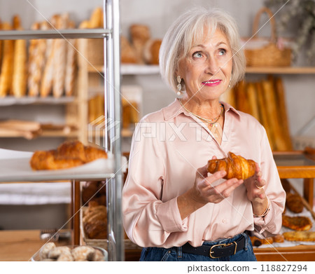 Mature woman in casual clothes chooses fresh croissants for breakfast in bakery 118827294