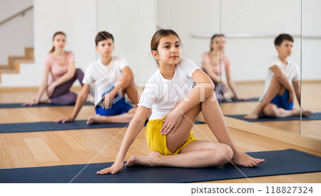 Girl practicing Matsyendrasana during family yoga training at gym Girl practicing Matsyendrasana during family yoga training at gym 118827324