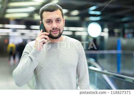 Male passenger in casual clothing talking on his mobile phone next to the subway escalator Male passenger in casual clothing talking on his mobile phone next to the subway escalator 118827371